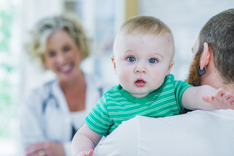 A father holds his baby during a visit to the doctor.