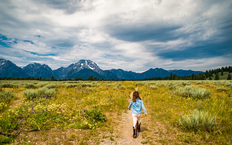 Girl walking on a path in a field with the Grand Tetons in the backgroud.