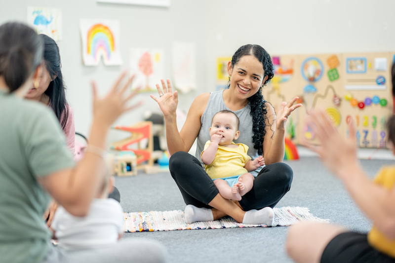 A small group of parents and their babies, participate in a sign language class together.  They are each dressed comfortably as they interact with their babies and learn new signs.